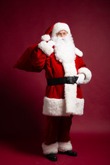 Portrait of grandfather in Santa Clause costume with gift sack on back posing on red background, Christmas and New year concept