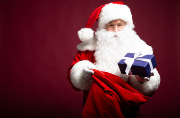 Happy Santa Clause giving present while holding with gift sack on red background, Christmas and New year concept