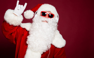 Funny and stylish Santa Clause holding smartphone and listening to music at headphone on red background, Christmas and New year concept
