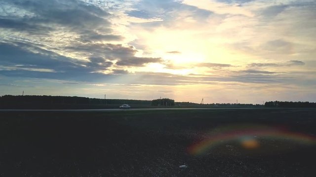 sunset light shines from behind clouds above road and field