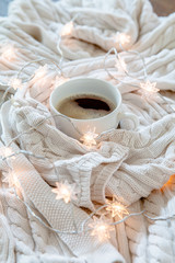 Obraz na płótnie Canvas Cup of coffee wrapped in whie cozy sweater with twinkle lights