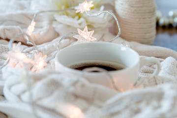 Cup of coffee wrapped in whie cozy sweater with twinkle lights