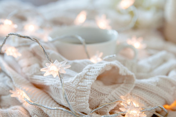 Cup of coffee wrapped in whie cozy sweater with twinkle lights