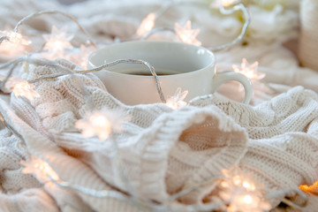 Cup of coffee wrapped in whie cozy sweater with twinkle lights