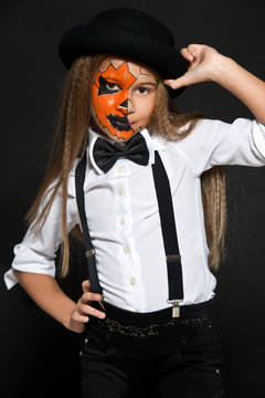 Funny child girl in pumpkin costume for Halloween. Halloween makeup. Face art.
