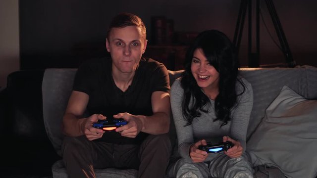 Couple playing videogame on console. Sitting on sofa at home. Girl wins.