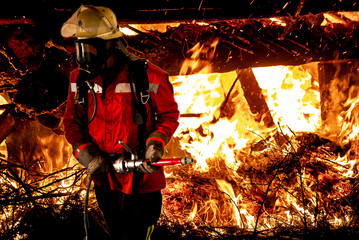 Feuerwehrmann mit Schlauchleitung und Atemschutzgerät vor einem Feuer