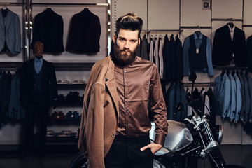 Elegantly dressed man with stylish beard and hair posing near retro sports motorbike at the men's clothing store.