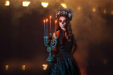 Portrait of a young woman with make-up for Halloween. She stands in the dark, holding a candlestick...