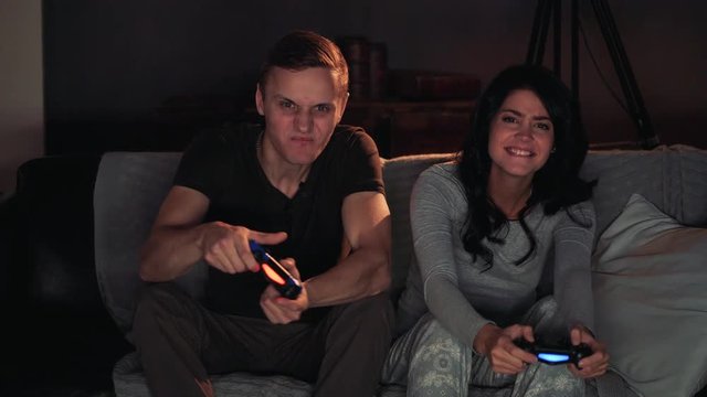 Couple playing videogame on console. Sitting on sofa at home. Men wins.