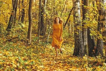 Young beautiful girl in a yellow long dress walks in autumn park with fallen leaves