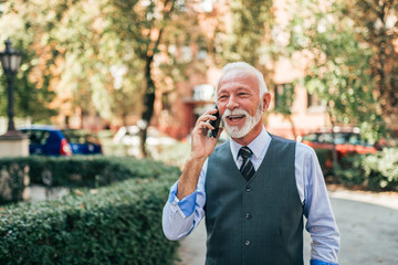 Smiling older businessman talking on the smartphone in the city street.