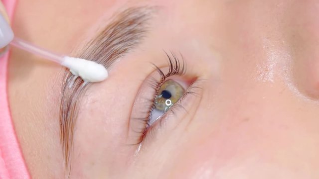 Cosmetic master using q-tip to clean eyebrows in a beauty salon.