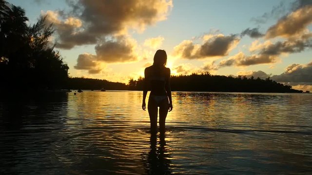 Girl standing in the water during sunset in French Polynesia. Woman Silhouette beautiful golden hour.