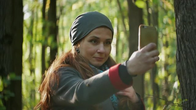 girl takes a selfie on the phone while walking in the forest among the trees