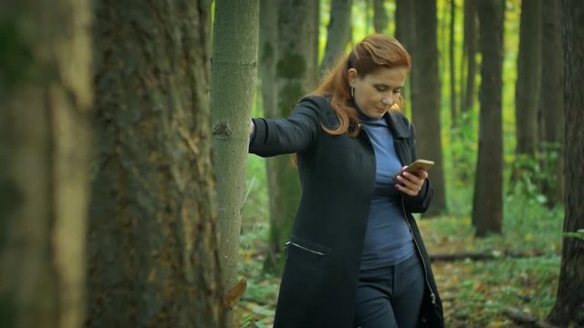 girl stands near the tree and writes sms on the phone