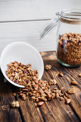 homemade granola in glass jar and scattered on a wooden table.