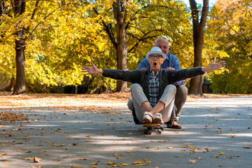 Senior man and woman having fun together while riding skateboard in autumn park