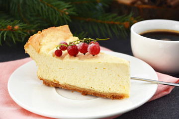 Cheesecake, decorated frozen red currant berries, and coffee cup on pine tree branch background. Christmas dessert with summer taste
