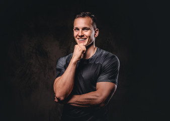 Portrait of a young handsome sportsman holds hand on chin on dark background.