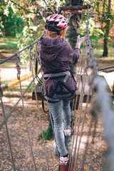 Naklejka premium wesoła dziewczyna, kobiety, sprzęt wspinaczkowy w parku przygód zajmują się wspinaczką skałkową po drodze linowej, arboretum, ubezpieczenie, atrakcja, park rozrywki, aktywny wypoczynek, autmn, zdjęcie pionowe