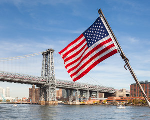 American Flag.  An American flag flies from a boat on the East River in New York City.  In the background is the Williamsburg Bridge connecting Manhattan and Brooklyn. - Powered by Adobe