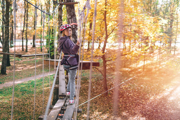 happy girl, women, climbing gear in an adventure park are engaged in rock climbing or pass obstacles on the rope road, arboretum, insurance, attraction, amusement park, active recreation, autmn, light