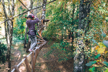 happy girl, women, climbing gear in an adventure park are engaged in rock climbing or pass obstacles on the rope road, arboretum, insurance, attraction, amusement park, active recreation, autmn