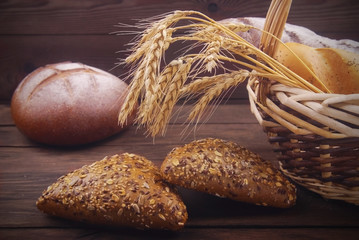 Bread and ears of wheat in a wheat basket on a wooden background with a light blur effect.