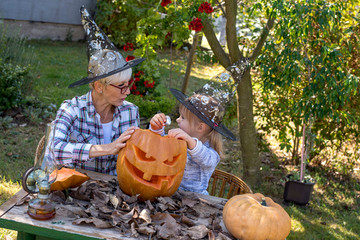 Smiling grandmother carving big pumpkin with her granddaughter and having fun together