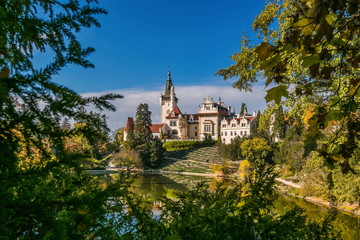 Obraz premium Scenic landscape of famous romantic Pruhonice castle, Czech Republic, Europe, standing on hill in a park, sunny colorful fall day, blue sky, spruce branches and maple leaves framing picture