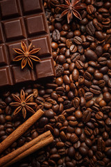 Texture spilling coffee beans, chocolate, cinnamon and cloves. Top view. Copy space.