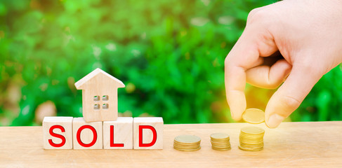 wooden house and coins with the inscription "sold". sale of property, home, real estate. affordable housing.