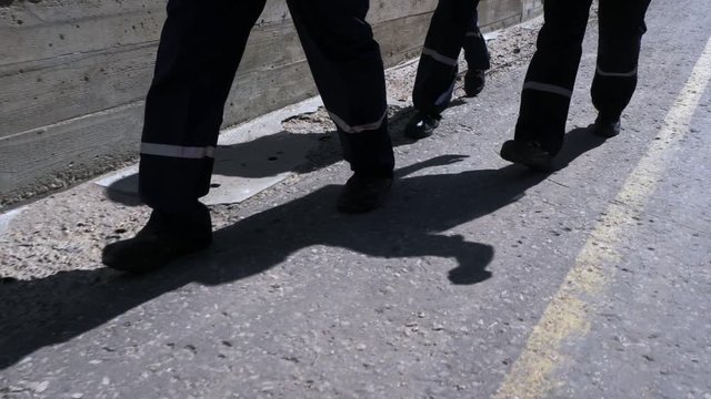 Feet and legs of workers in overalls walking down road markings
