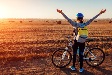 Happy young bicyclist raising opened arms in autumn field admiring the view. Woman feeling free.