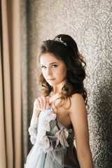 Portrait of a cute bride in a wedding dress near the window. Wedding morning