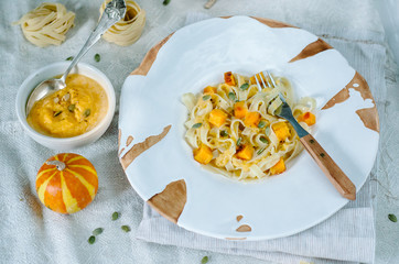 Pasta with pumpkin in a cream sauce in a craft bowl. Handmade ceramic plate. Autumn meal for lunch.
