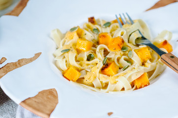 Pasta with pumpkin in a cream sauce in a craft bowl. Handmade ceramic plate. Autumn meal for lunch.