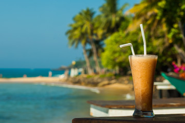 Glass with fruit juice fresh on the background of the sea and palm trees
