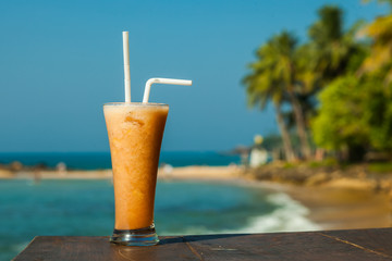 Glass with fruit juice fresh on the background of the sea and palm trees