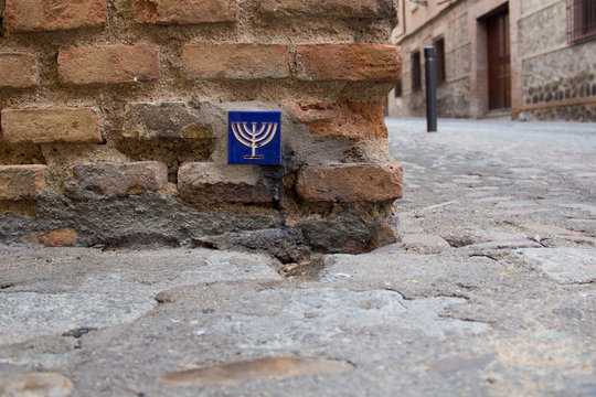 A blue pottery tile with a yellow menorah on it in a brick wall in the Jewish quarter of Toledo, Castile-La Mancha, Spain, a UNESCO World Heritage Site