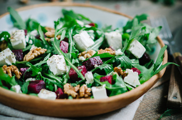 Salad with beets, walnuts, feta cheese and arugula. Rustic style salad on a dark wooden background
