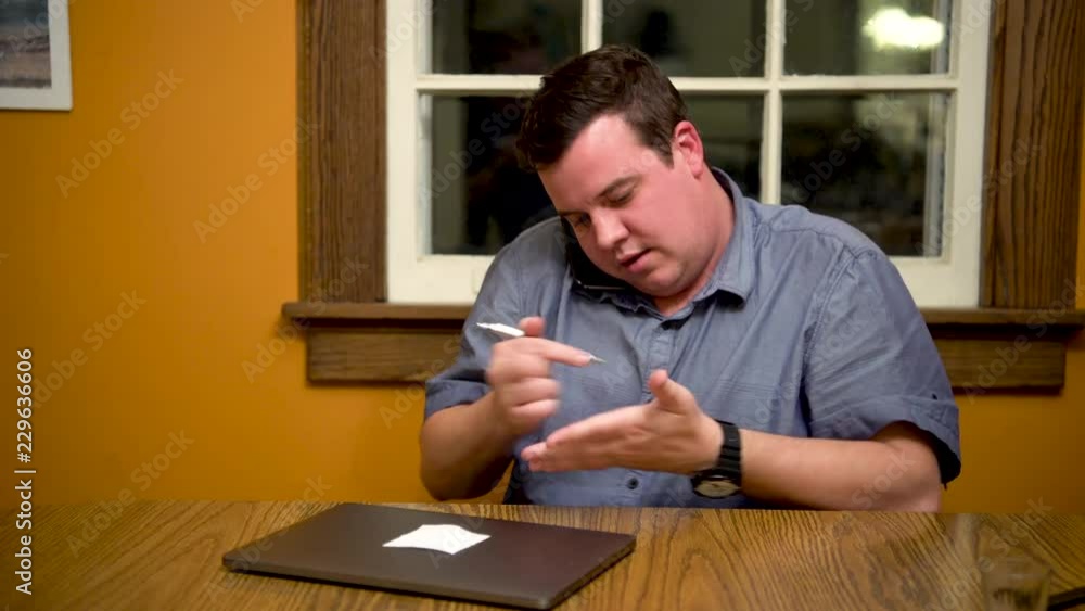 Poster man at desk answers phone and quickly and confidently takes notes on his hand with a pen.