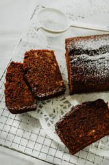 Chocolate cake with nuts inside cut into slices on cooling rack. A mini sieve with powdered sugar. Directly above, white background.