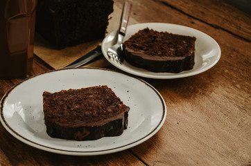Chocolate pound cake pieces on white plates. Brown toned, wooden background.