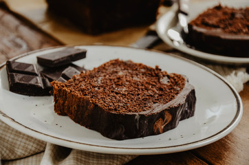 Chocolate pound cake slices on white plates. Brown toned, wooden background. Chocolate bar broken into pieces.