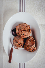 Homemade chocolate ice cream in a bowl with a rustic spoon. Directly above, white background.