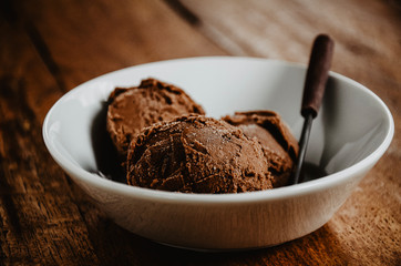 Homemade chocolate ice cream in a bowl with a spoon. Low view shot, close up, dark wooden background.