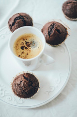 Mini chocolate muffins on white plate with a cup of coffee in the middle. High angle shot, white background.
