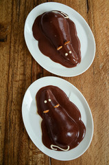 Pear halves coated with chocolate glaze and decorated like a mouse. Creative food, funny dessert for picky eaters. Directly above, wooden table background.